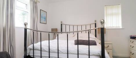 A single bed with a metal frame, a bedside table, a nightstand, a window with blinds, and a hanging light fixture.