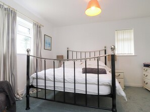 A single bed with a metal frame, a bedside table, a nightstand, a window with blinds, and a hanging light fixture. - Belan Wen (Beaumaris)