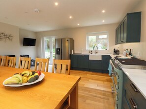 A modern kitchen with a dining area, wooden chairs, a table with fruit, a TV, and a window with a view. - Belan Wen (Beaumaris)