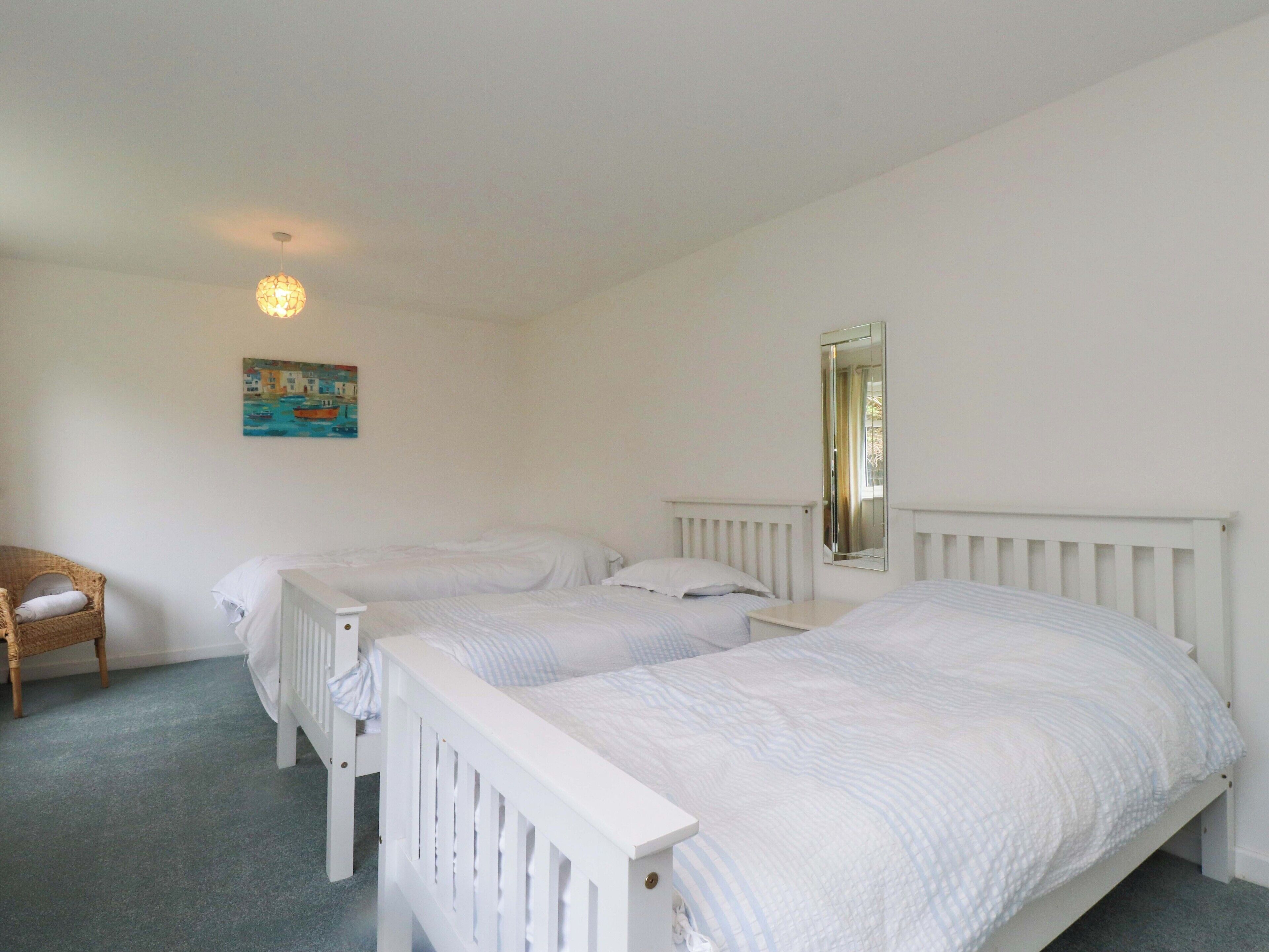 Une chambre avec deux lits simples, un radiateur blanc, un miroir fixé au mur et un tableau représentant un paysage côtier.