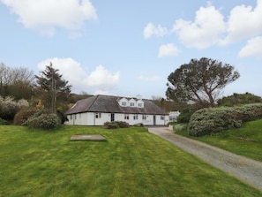 A white building with a grey roof, surrounded by green grass and trees.
