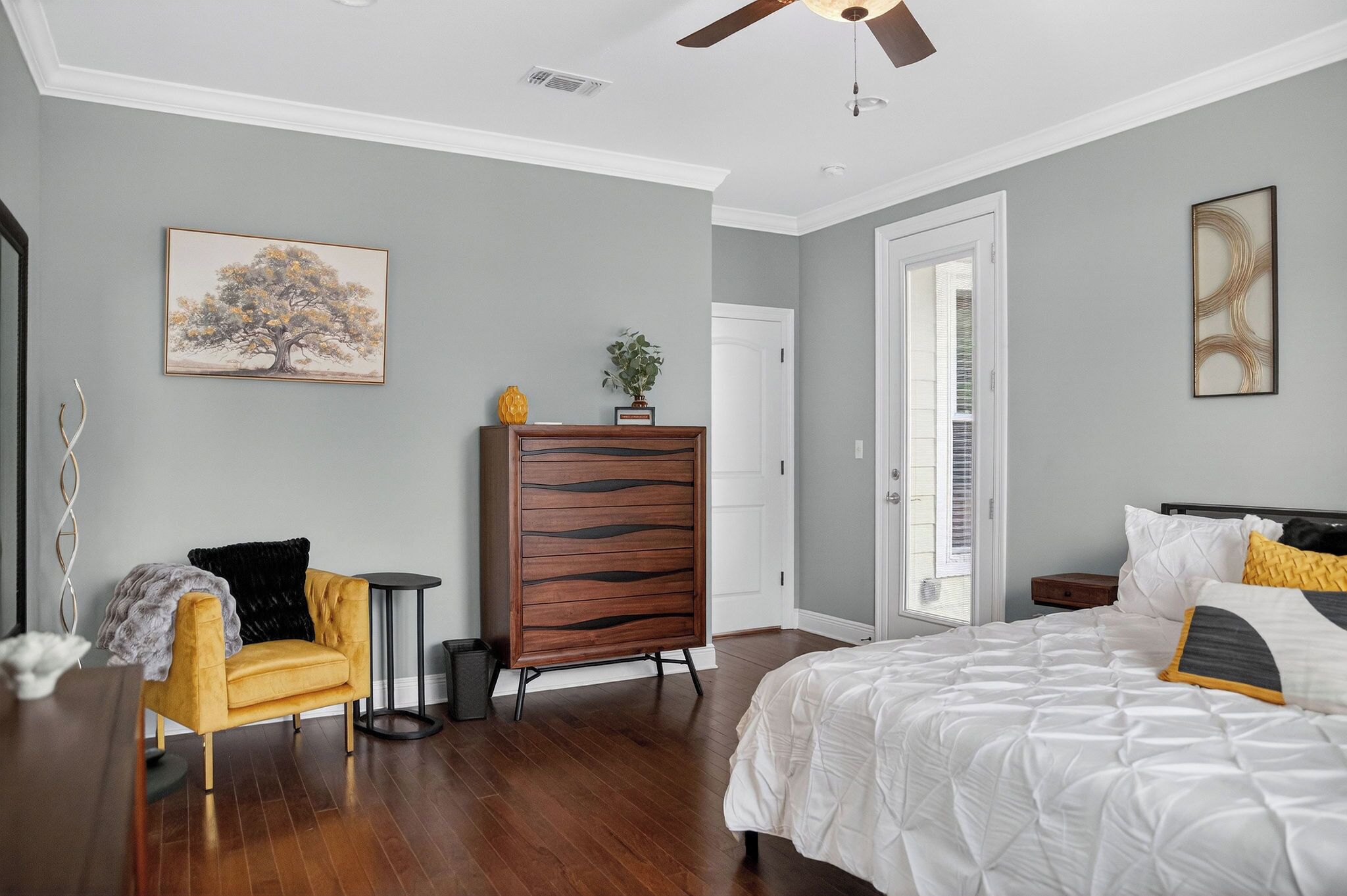 A bedroom with a bed, a dresser, a chair, a small table, and a painting on the wall.