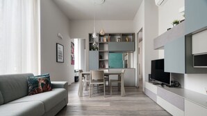 Ein modernes Wohnzimmer mit einer Couch, einem Esstisch und einem an der Wand befestigten Fernseher.