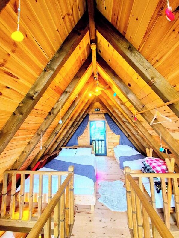 An attic bedroom with a sloped ceiling, wooden beams, a bed, a window, and a door.