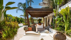 Un espace de détente extérieur baigné de lumière, avec des sièges confortables, une pergola et des plantes en pot.