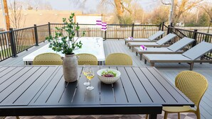 A deck with a table, chairs, a hot tub, and lounge chairs.