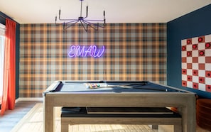 Una mesa de billar en una habitación con papel tapiz escocés, un letrero de neón y un patrón de pared a cuadros.