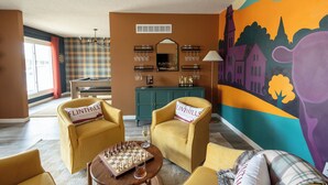 A cozy room with a billiards table, two armchairs, a coffee table with a chess set, and a mural on the wall.