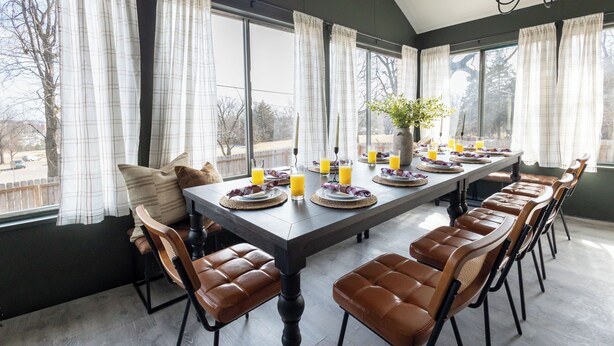 A dining area with a long table set for six, surrounded by brown leather chairs, with a vase of flowers and plates of food and drinks.