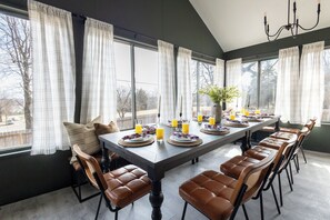A dining area with a long table set for six, surrounded by brown leather chairs, with a vase of flowers and plates of food and drinks.