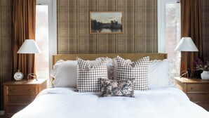 A hotel room with a checkered bedspread, a painting on the wall, and a view of the outdoors through the window.