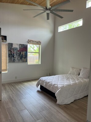 Ein Schlafzimmer mit Bett, Deckenventilator, Fenster mit Jalousien und einem Bild an der Wand.