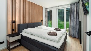 Un dormitorio moderno con cama, mesita de noche y vistas al exterior con vegetación.