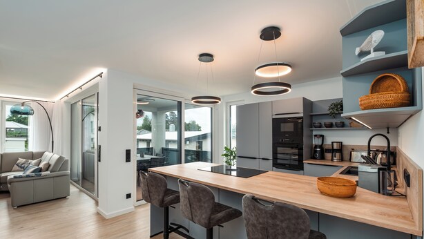 Una cocina moderna con una isla central, taburetes de bar y estantes empotrados.