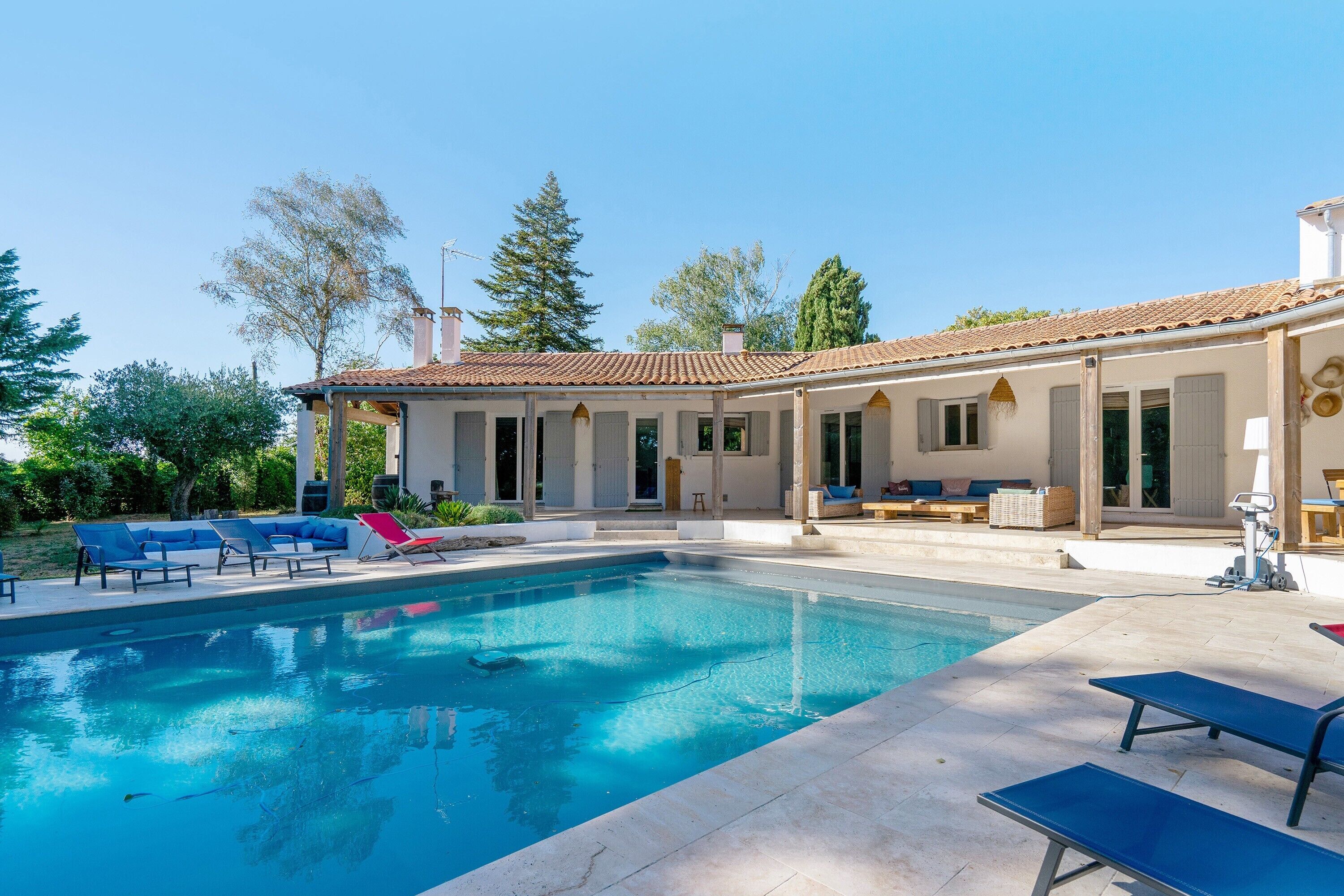 A pool with lounge chairs, a covered patio, and a building with columns and a tiled roof.