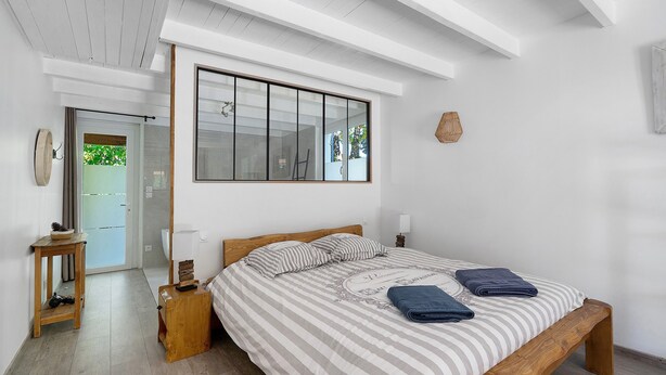 A bedroom with a large window, a wooden bed frame, a bedside table, and a nightstand. - Large Villa with Private Pool, Balcony and Wi-Fi in Saint-Georges des Coteaux (Saint-Georges-des-Coteaux)