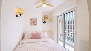 Um quarto com cama, ventoinha no teto, luminária na parede, janela e varanda.
