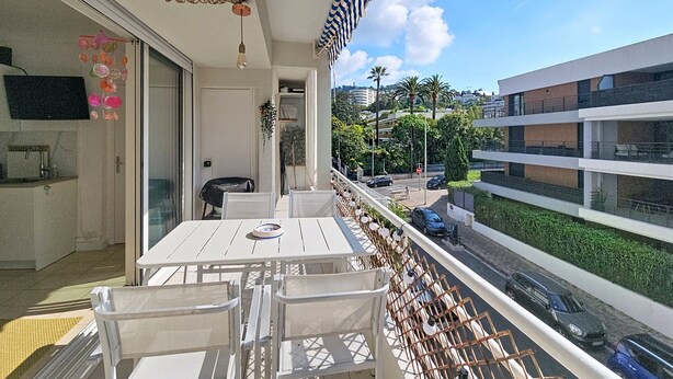 Uma varanda com mesa e cadeiras, vista para a rua e um edifício com vários andares.