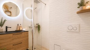 Um banheiro moderno com box de vidro, bancada de madeira, espelho redondo com iluminação e vaso sanitário.