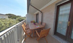 A balcony with a wooden table and chairs, a potted plant, and a view of greenery. - Familiar Seaside Apartment in Lignano (Lignano Sabbiadoro)