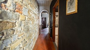 A corridor with stone walls, a tiled floor, and an archway leading to another room. - Elegant Penthouse in the heart of Santo Spirito (Firenze)