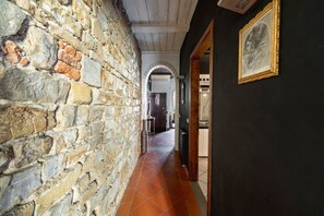 A corridor with stone walls, a tiled floor, and an archway leading to another room. - Elegant Penthouse in the heart of Santo Spirito (Firenze)