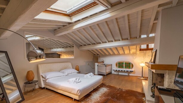 A bedroom with a bed, a mirror, a lamp, a fireplace, and a cowhide rug. - Elegant Penthouse in the heart of Santo Spirito (Firenze)