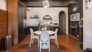 A modern kitchen with a round dining table, white chairs, a stone archway, and a hanging light fixture. - Elegant Penthouse in the heart of Santo Spirito (Firenze)