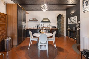 A modern kitchen with a round dining table, white chairs, a stone archway, and a hanging light fixture. - Elegant Penthouse in the heart of Santo Spirito (Firenze)
