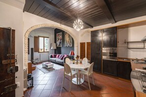 A kitchen with a dining area, a fireplace, and a stone archway leading to a living room. - Elegant Penthouse in the heart of Santo Spirito (Firenze)