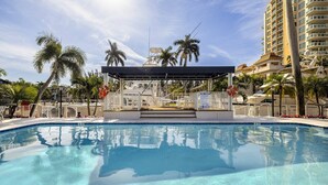 A clear swimming pool with a covered area, palm trees, and a high-rise building in the background. - Spacious 2-Bedroom Suite Just Steps from Famous Fort Lauderdale Beach (Fort Lauderdale)