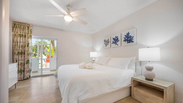 A bedroom with a bed, bedside lamps, a ceiling fan, and a view of the outdoors. - Spacious 2-Bedroom Suite Just Steps from Famous Fort Lauderdale Beach (Fort Lauderdale)
