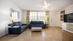 A living room with a sofa, a coffee table, a TV, and a ceiling fan. - Spacious 2-Bedroom Suite Just Steps from Famous Fort Lauderdale Beach (Fort Lauderdale)