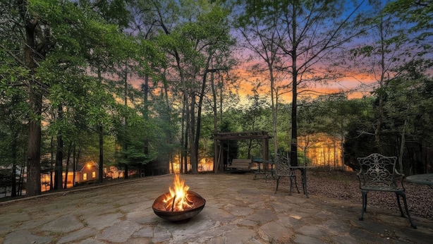 A stone patio with a fire pit, surrounded by trees and a gazebo. - Charming Waterfront Retreat. deep-water dock (Gainesville)