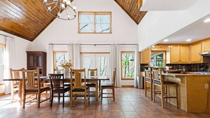 A spacious kitchen with wooden cabinets, a dining area with a table and chairs, and large windows with artwork. - Charming Waterfront Retreat. deep-water dock (Gainesville)