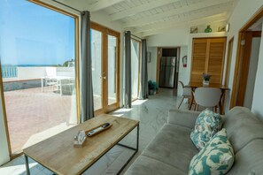 A spacious living area with a sofa, a coffee table, and a dining table. Large windows provide a view of the outdoors. - Rooftop Ocean View | Historic Old San Juan (San Juan)