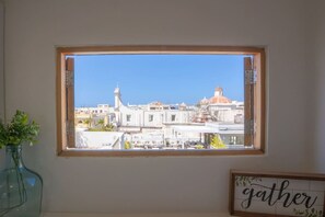 A window with a view of a cityscape, a framed sign with the word 'gather,' and a vase with green plants. - Rooftop Ocean View | Historic Old San Juan (San Juan)