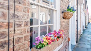 A narrow street with a brick building, a window with a flower box, and a hanging planter with flowers. - Luxury Victorian Terrace Inside City Walls (York)