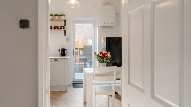 A modern kitchen with white cabinetry, a coffee machine, and a vase with flowers on the table. - Luxury Victorian Terrace Inside City Walls (York)