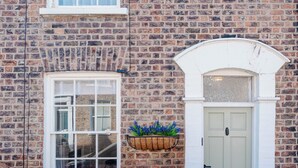 A brick building with a white door, a window, and a hanging planter with blue flowers. - Luxury Victorian Terrace Inside City Walls (York)