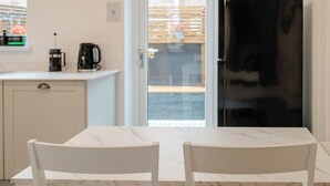 A white marble table with two white chairs, a black coffee maker, and a white cabinet in a kitchen with a glass door leading outside. - Luxury Victorian Terrace Inside City Walls (York)
