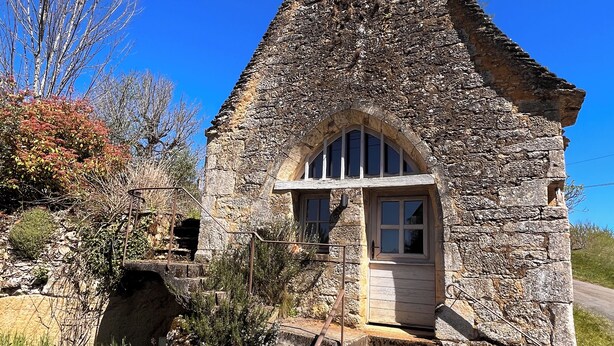 Une petite maison en pierre avec une porte en bois, une petite fenêtre et un escalier en pierre menant à l’entrée.