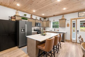 Une cuisine moderne avec des meubles en bois, un îlot central doté de tabourets, un réfrigérateur, un four à micro-ondes et un évier.