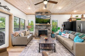 Un salon chaleureux avec une cheminée en pierre, un plafond en bois et une grande fenêtre.