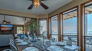A dining area with a view of the ocean, a ceiling fan, and a TV on the wall. - Stunning Bayfront Home!  Panoramic Views, Fishing, Crabbing and Epic Sunsets. (Jamaica Beach)