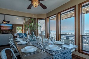 A dining area with a view of the ocean, a ceiling fan, and a TV on the wall. - Stunning Bayfront Home!  Panoramic Views, Fishing, Crabbing and Epic Sunsets. (Jamaica Beach)