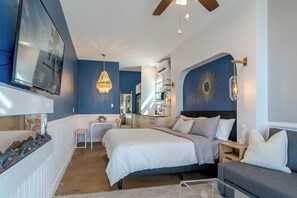 A bedroom with a bed, bedside tables, a desk, a chair, a chandelier, and a wall-mounted TV. - Stunning Bayfront Home!  Panoramic Views, Fishing, Crabbing and Epic Sunsets. (Jamaica Beach)