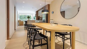 Een moderne eetruimte met een houten tafel en zwarte stoelen, een hangende hanglamp en een ronde spiegel aan de muur.