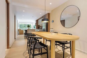 Een moderne eetruimte met een houten tafel en zwarte stoelen, een hangende hanglamp en een ronde spiegel aan de muur.