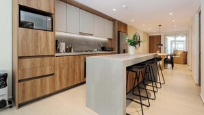 Een moderne keuken met houten kastjes, een centraal eiland met barkrukken, en een zithoek met een bank en tafel.